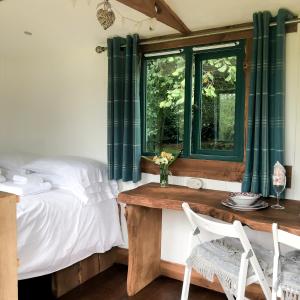 a bedroom with a bed and a table and a window at Shire the Shepherd's Hut at Pentref Luxury Camping in Penuwch