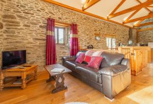 a living room with a leather couch and a tv at The Threshing Barn in Gwennap