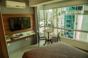 een slaapkamer met een bed en een raam met een televisie bij Para casais, prédio beira mar, em frente à Roda Gigante in Balneário Camboriú