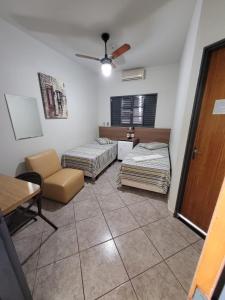 a room with two beds and a chair and a table at Hotel Graunas in São Carlos