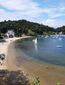 a beach with a sail boat and people in the water at Angra dos Reis, Bonfim Cond Refúgio do Corsário in Angra dos Reis