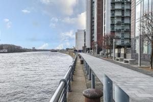 a walkway next to a river next to buildings at Riverside Modern 2 Bedroom Flat in Glasgow