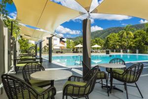 a patio with tables and chairs and a swimming pool at Belle Escapes Tranquil Waters Luxury Home Palm Cove in Palm Cove