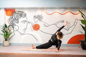 une femme faisant une pose de yoga devant une fresque dans l'établissement Selina Brighton, à Brighton et Hove
