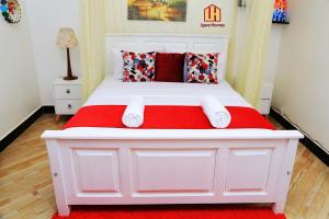 Cama blanca con manta roja y almohadas en Igwe Homes - Kisaasi en Kampala