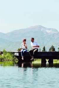 Ein Mann und eine Frau sitzen auf einem Dock über dem Wasser in der Unterkunft Winterstellgut in Annaberg im Lammertal