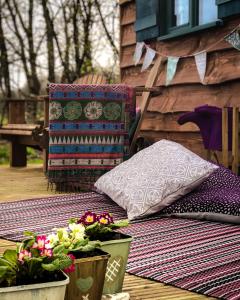 a blanket and pillows on a deck with flowers at Shire the Shepherd's Hut at Pentref Luxury Camping in Penuwch
