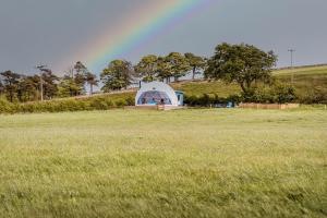 a tent in a field with a rainbow in the background at The Dome at Mid Auchengowan in Lochwinnoch