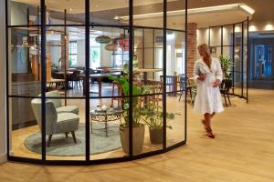 een vrouw in een witte jurk loopt in een kamer met glazen wanden bij Ringhotel Landhaus Gardels in Sankt Michaelisdonn