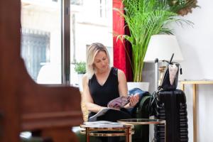 a woman sitting in a chair looking at a book at Hôtel Churchill Bordeaux Centre in Bordeaux
