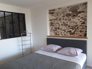 un lit avec deux oreillers dans une pièce avec un mur en pierre dans l'établissement Les Palmiers. Charme, spa et massage en vignoble nantais, au Pallet 15 autres photos