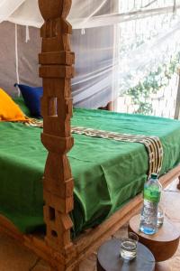 ein Bett mit einer grünen Decke und einer Flasche auf dem Tisch in der Unterkunft Maison Pierres in Toubab Dialao