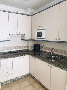 a kitchen with white cabinets and a sink and a microwave at Hostal Tres Soles in Nerja