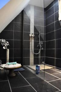 een badkamer met een douche in een zwart betegelde muur bij Oelde Apartment in Oelde
