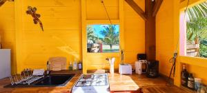 une cuisine jaune avec un évier et une fenêtre dans l'établissement Yuka Lodge - Bungalow privé avec jardin en pleine nature, à Sainte-Anne