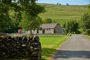 a stone wall in front of a field with a barn at Littondale Country & Leisure Park in Skipton