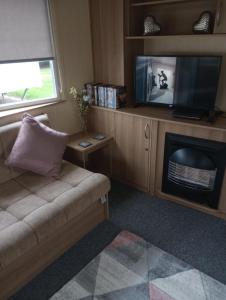 ein Wohnzimmer mit einem Sofa und einem TV in der Unterkunft A22 is a 3 bedroom caravan on Whitehouse Leisure Park in Towyn near Abergele with decking and close to sandy beach in Conwy