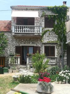a stone house with a balcony and flowers in front of it at Apartments Martinac in Sukošan