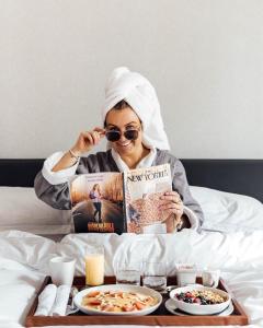 una mujer sentada en la cama leyendo un libro y comiendo comida en Kimpton Saint George Hotel, an IHG Hotel, en Toronto