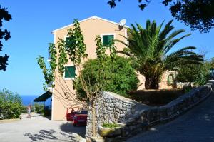 a house with a palm tree and a stone wall at Heliovasilema (Sunset) Apartments and Studios in Fiskardho