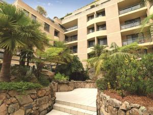 a building with a stone wall and palm trees and a walkway at Adina Apartment Hotel Coogee Sydney in Sydney