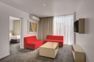 ein Wohnzimmer mit 2 roten Stühlen und einem TV in der Unterkunft Travelodge Hotel Melbourne Docklands in Melbourne