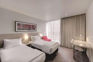 a hotel room with two beds and a desk at Travelodge Hotel Melbourne Docklands in Melbourne