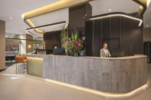 a woman standing at a reception desk in a lobby at Vibe Hotel Melbourne in Melbourne