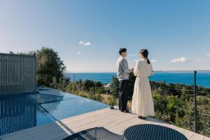 un hombre y una mujer de pie en un balcón con vistas al océano en WEAZER 西伊豆 en Izu