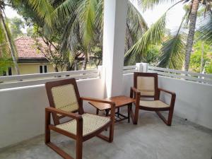 two chairs and a table on a balcony with palm trees at Gloria Inn in Negombo