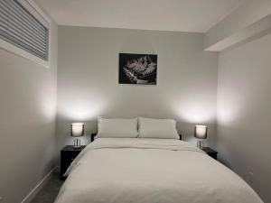 a white bedroom with a bed and two lamps at Cozy New Suite in NW Calgary in Calgary