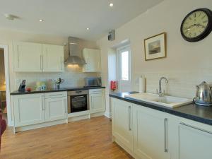 uma cozinha com armários brancos e um relógio na parede em Lapwing Cottage - E5028 em Birtley