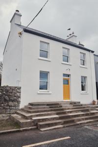 a white house with a yellow door and stairs at Contemporary yet cosy and characterful home in rural village setting in Kilfenora