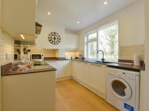 a kitchen with white cabinets and a washer and dryer at Pillhead Cottage in Westleigh