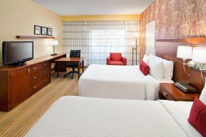 a hotel room with two beds and a desk and a television at Courtyard by Marriott Albuquerque Airport in Albuquerque