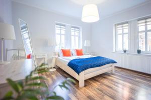 a white bedroom with a bed with blue sheets and orange pillows at Apartament na deptaku, MyWeek in Polanica-Zdrój