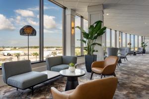 Tampa Airport Marriott في تامبا: غرفة انتظار مع كراسي وطاولات ونوافذ كبيرة
