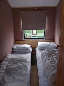 twee bedden in een kleine kamer met een raam bij Melody Brooks Caravan Park in Portknockie