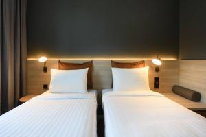 2 camas en una habitación de hotel con sábanas blancas en Moxy Stuttgart Feuerbach en Stuttgart