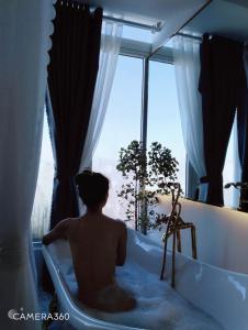 a man sitting in a bath tub looking out a window at AMIGO Luxury Palace- Cạnh Chợ Đêm Đà Lạt in Da Lat