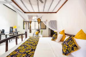 a room with a white bed with yellow pillows at Zarafa House in Diani Beach
