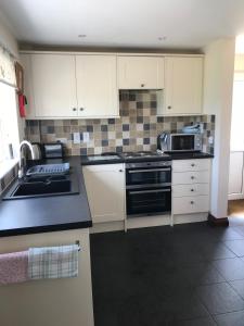 una cocina con armarios blancos y electrodomésticos negros en Willow cottage, romantic retreat near Honiton Devon en Honiton