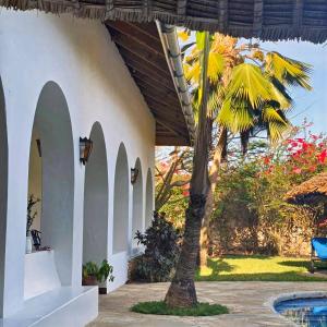 a palm tree next to a building with a pool at Zarafa House in Diani Beach