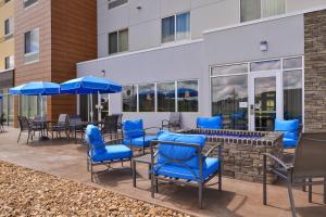 ウォレンズバーグにあるFairfield Inn & Suites by Marriott Warrensburgの青い椅子とテーブル、パラソル付きのパティオ