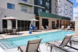 una piscina con sillas y sombrillas en un hotel en Courtyard by Marriott Dallas Plano/The Colony, en The Colony