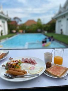 een tafel met een bord ontbijtproducten en een zwembad bij Bianco House Resort in Cha Am