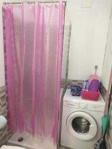 El baño incluye una cortina de ducha rosa sobre una lavadora. en Estudio La Luna en Bajamar