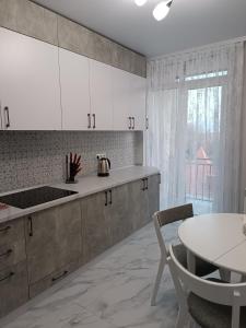 une cuisine avec des placards blancs, une table et une fenêtre dans l'établissement Apartments Domovik Трьохкімнатна квартира , європейського стилю, à Moukatcheve