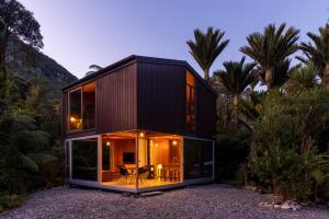 a black house with glass walls and trees at Punakaiki Forest Retreat in Punakaiki