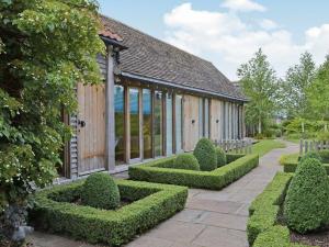 un edificio con una fila de setos en un jardín en The Barn At Butts Farm, en Wicken